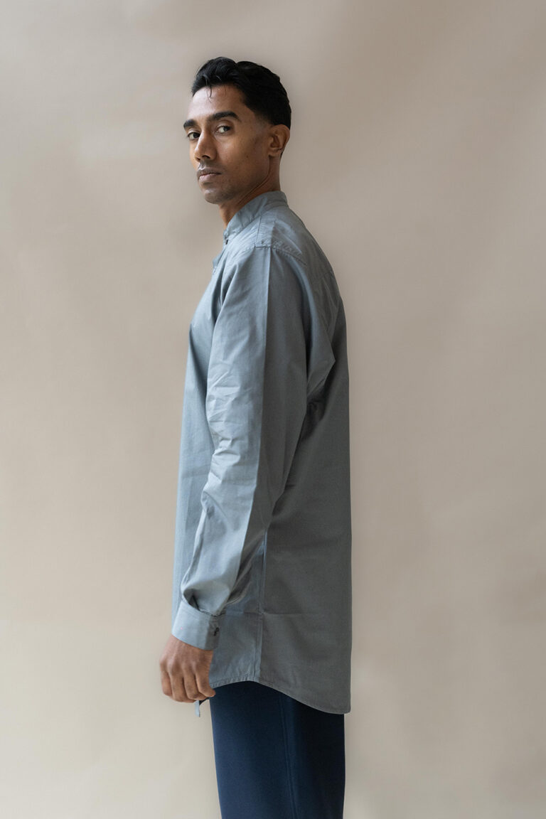 Man in grey shirt posing side-view against neutral background.