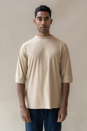 Man in beige T-shirt standing against neutral background.